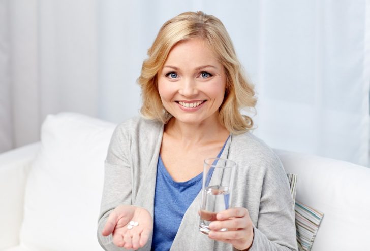 happy woman with glass of water takes pill