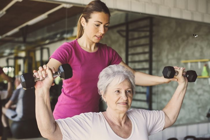 older woman lilflting weights with trainer